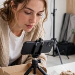 Content creator filming a product unboxing on a smartphone in a bright studio with softbox lighting